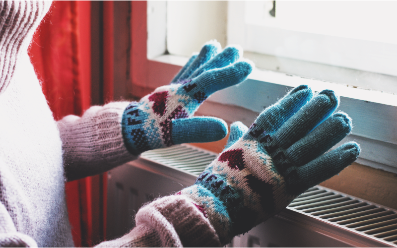 Image of a person wearing gloves with their hands over a radiator
