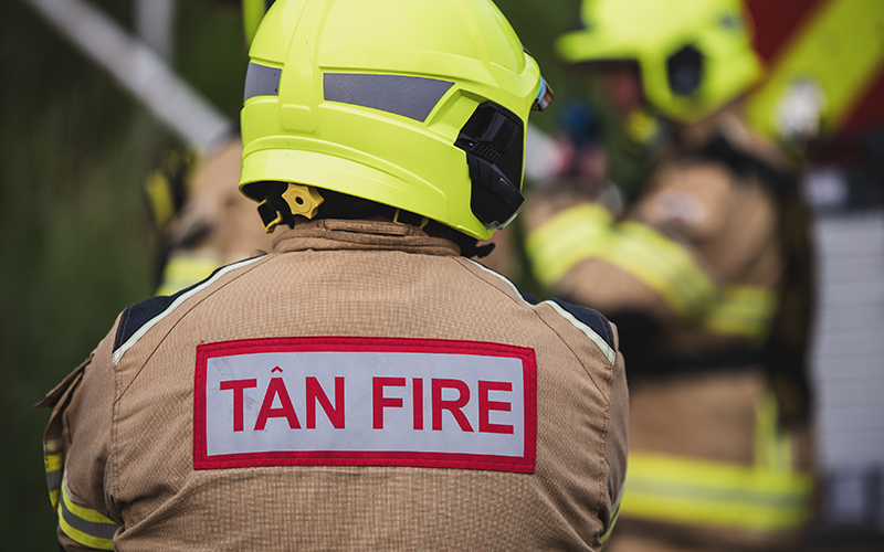 The back of a fire person wearing a helmet and a jacket with the wording  Tan/ fire on it