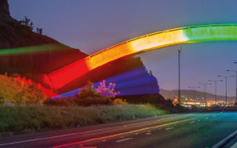 Photograph of a bridge lit up with neon rainbow lights