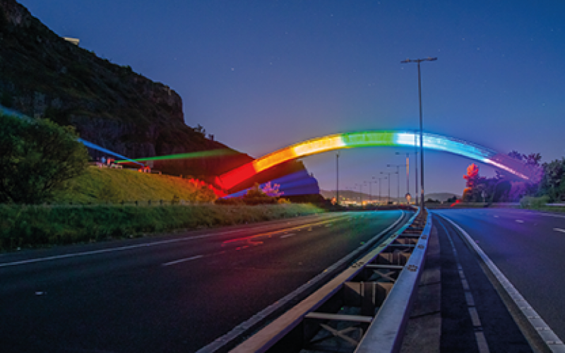 Photograph of a bridge lit up with neon rainbow lights