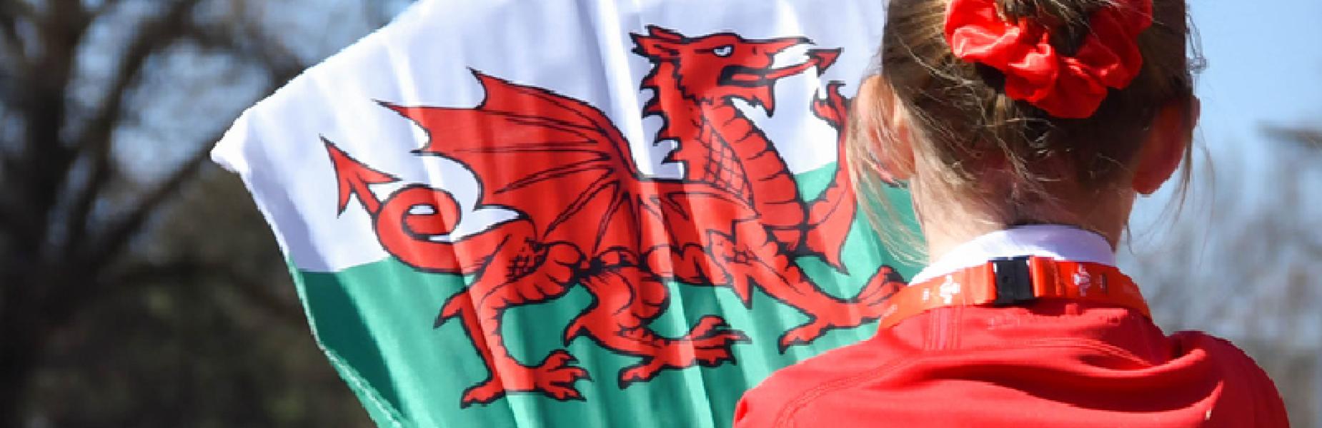 Merch ifanc yn gwisgo top coch yn dal baner Cymru